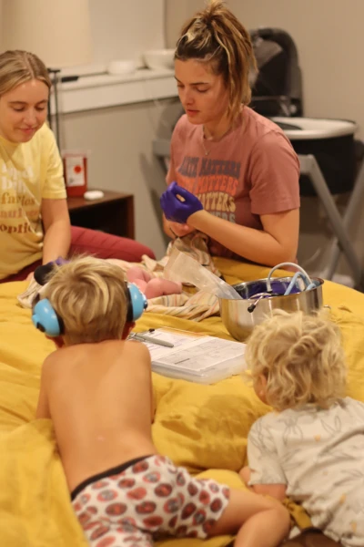 Midwife Caroline Sausler completes a newborn exam on a bed after a home birth while an assistant midwife and two older children look on
