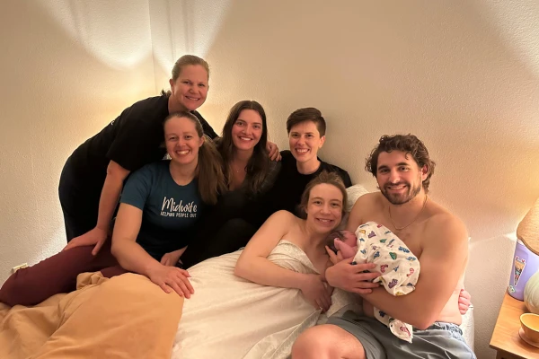 Caroline Sausler and Rachel Wright pose smiling with the Northshore midwives and a family who just had a homebirth